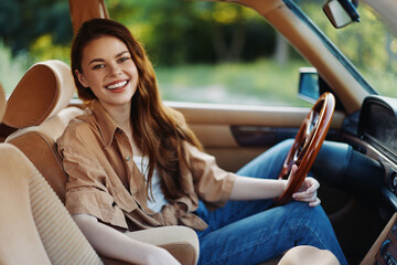 Poster - Joyful young woman smiling inside a vintage car, dressed in casual attire with a warm color palette, perfect for lifestyle and travel concepts.