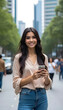 © Alexbedoya - Smiling young woman holding a smartphone in an urban environment..