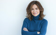 © Aleena  - A beautiful woman in her late thirties, wearing a blue turtleneck sweater, is smiling with her arms crossed over her chest, posing for a photo on a plain background.