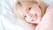 © Phanupong - Smiling woman with blonde hair lying on a white bed in sunlight