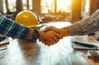 © Ada - yellow safety helmet on workplace desk with construction worker team hands shaking greeting start up plan new project contract in office center at construction site, partnership and contractor concept