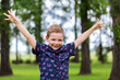 © Austockphoto - Portrait of kindergarten aged boy outdoors smiling with arms wide in celebration of success