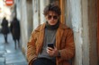 © PD - Young man in sunglasses checks smartphone while leaning against wall in urban setting during daylight hours