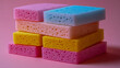 © photolas - Vibrant kitchen sponges stacked in a playful arrangement against a pink background