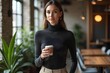 © NISHAN'S STUDIO - A woman wearing a fitted turtleneck sweater, wide-leg trousers, and statement earrings, holding a cup of coffee in a chic, industrial-style office space