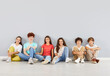 © Studio Romantic - Group of happy students or friends sits together on the floor for a fun portrait on a grey background. The kids are enjoying time as a team, friendship and unity in this diverse and lively setting.