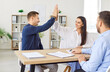 © Studio Romantic - Couple of clients celebrating an agreement with a high five after purchasing real estate with consultant in an office. The moment reflects satisfaction and excitement over a profitable investment.