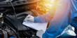 © sorapop - Skilled Asian mechanic in blue shirt writing on a paper while working on a car in an auto repair shop. Close-up shot of hand.