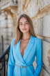 © larrui - Confident young woman in a vibrant blue blazer posing elegantly near classic architectural details
