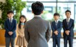 © Raffaza - Businessman addressing children in suits in an office setting