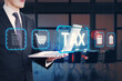 © Who is Danny - Businessman holding laptop with tax-related digital icons on futuristic background.