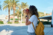 © Lazy_Bear - Female traveler in casual clothing taking picture in coastal town. Woman using orange retro instant camera to take photo during vacation. Tourist captures memories during travel