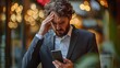© Wilasinee - A businessperson with a worried expression hand on forehead contemplating news or information displayed on their smartphone as they face a challenge or difficulty