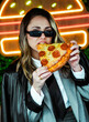 © dolores - Joven empresaria comiendo pizza frente a luces de neón en la calle