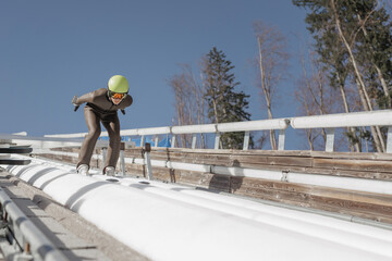 Ski jumper sitting on a start bar on top of ski jump focusing on speeding up down the inrun track. Winter sports concept.