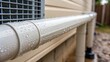 © DigitalSpace - A medium closeup of a condensate drain line connected to an air conditioning unit featuring the smooth PVC pipe with condensation beads forming along the exterior exemplifying the