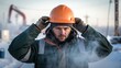 © DigitalSpace - A medium closeup of a worker adjusting their hard hat their breath visible in the cold air conveying the stark differences between safety procedures and extreme weather.