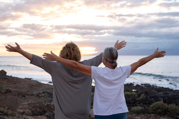 Sticker - Back view of mature and senior women standing face to the sea with outstretched arms looking at horizon over water, couple of females stay together enjoying freedom and vacation or retirement