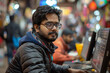 © TesaI - Young indian programmer works late at night in a busy office, focused on coding tasks amidst glowing screens and technology