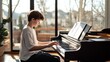 © olga_demina - Young boy practicing piano and reading sheet music in front of a large window, immersed in his passion for music while developing skills and enjoying a serene moment at home