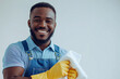 © PeterStone - Portrait Black Smiling Man Cleaning Service Worker In Yellow Gloves, Holds White Cleaning Cloth, Light Blue Uniform And Blue Overalls