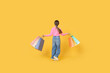 © Prostock-studio - A young girl in casual attire joyfully walks while holding colorful shopping bags. She has long hair and wears a pink top with denim jeans, set against a vibrant yellow background.