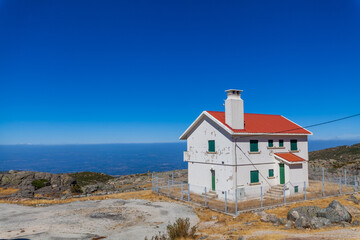 Wall Mural - A white house with a red roof sits atop a rocky mountain overlooking a vast landscape under a clear blue sky