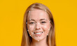 © Prostock-studio - A young woman with long hair smiles confidently against a vibrant yellow background. Her face is overlaid with digital points, demonstrating facial recognition technology.