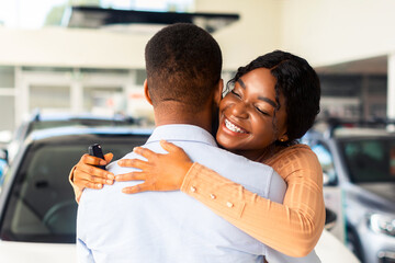 Wall Mural - Grateful Black Wife Embracing Husband After Buying Car In Dealership Showroom, Happy African American Woman Thankful For Purchasing New Automobile, Cheerful Lady Holding Keys And Smiling, Closeup