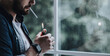© Prostock-studio - Suffering some problem, feeling desperate, crisis and depression. Habit and addiction. Sad millennial bearded guy lights cigarette with lighter, on window background, cropped, panorama, copy space