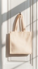Poster - Beige tote bag mockup hanging on a white door, with soft window light casting gentle shadows, ideal for displaying unique designs and branding concepts in a minimalistic setting