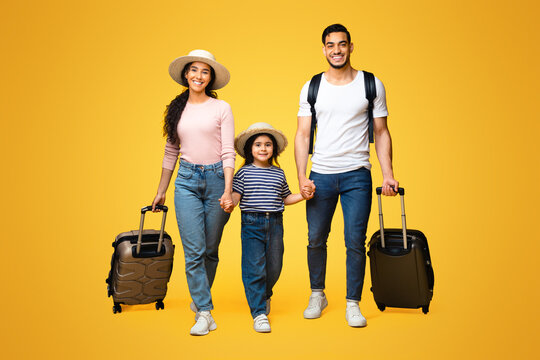 Happy Arab Family Of Three Holding Hands And Walking With Suitcases On Yellow Studio Background, Cheerful Middle Eastern Parents With Little Daughter Ready For Vacation Trip, Full Length Shot