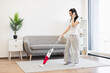 © sofiko14 - Asian female in casual attire vacuuming living room while listening to music, creating relaxed home atmosphere.