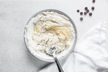 Wall Mural - Overhead view of flour being folded into cookie dough, top view of cookie dough being mixed in a grey bowl, process of making cookie dough or chocolate chip cookie dough