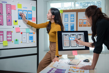 Two female web designers engaging in a lively discussion about user interface design for a mobile application, utilizing a whiteboard and computer in a collaborative office environment