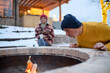 © Halfpoint - Older man starting fire in garden fire pit. Seniors watching flames, relaxing and drinking hot tea.