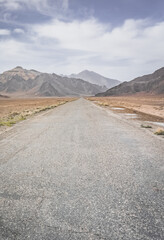 Wall Mural - Asphalt road of the Pamir Highway in the valley of the Tien Shan Mountains in Tajikistan in the Pamirs, landscape in the high desert mountains for background, the road goes into the distance