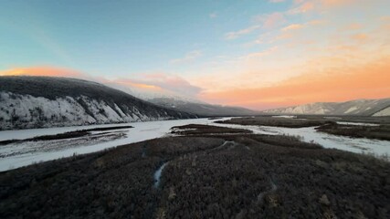 Wall Mural - A stunning view captures the beauty of a winding river surrounded by snow-covered mountains during sunset. The vibrant colors illuminate the serene winter landscape.