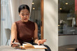 © bongkarn - An attractive Asian woman takes notes in a book or writes in her diary while relaxing in a cafe.