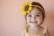 © Philippova - Smiling toddler wearing a sunflower headband with a cheerful expression against a soft peach background