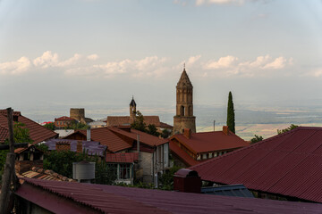 Wall Mural - A town with a red roof and a tall tower. The sky is cloudy and the sun is setting