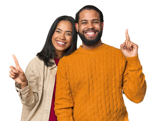 Wall Mural - Young Latino couple in studio indicates with both fore fingers up showing a blank space.