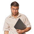 © Asier - Man holding laptop, studio confused, feels doubtful and unsure.