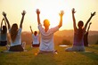 © WoodHunt - A group of friends is participating in a fun outdoor yoga class on a grassy field. The sun is setting behind them, creating a peaceful and serene atmosphere