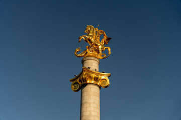 A gold statue of a dragon on top of a tall column. The sky is blue and clear