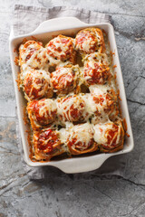 Wall Mural - Hot appetizer garlic sliders stuffed with meatballs, topped with tomato sauce and grated cheese close-up in a baking dish on a table. Vertical top view from above