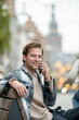 © Connect Images - A young man with a beard is sitting on a bench outdoors, smiling while talking on his phone, Nijmegen, Netherlands