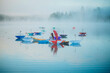 © Connect Images - A serene lake with colorful open umbrellas floating on the water, surrounded by misty fog and a forest backdrop, creating a whimsical and peaceful atmosphere, Wildcat Lake, WA, USA