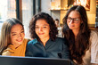 © Connect Images - Three women closely gathered around a laptop, intently reviewing content on the screen with a warm indoor lighting, Berlin, Germany