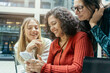 © Connect Images - Three smiling women sharing a moment while looking at a smartphone together, Berlin, Germany